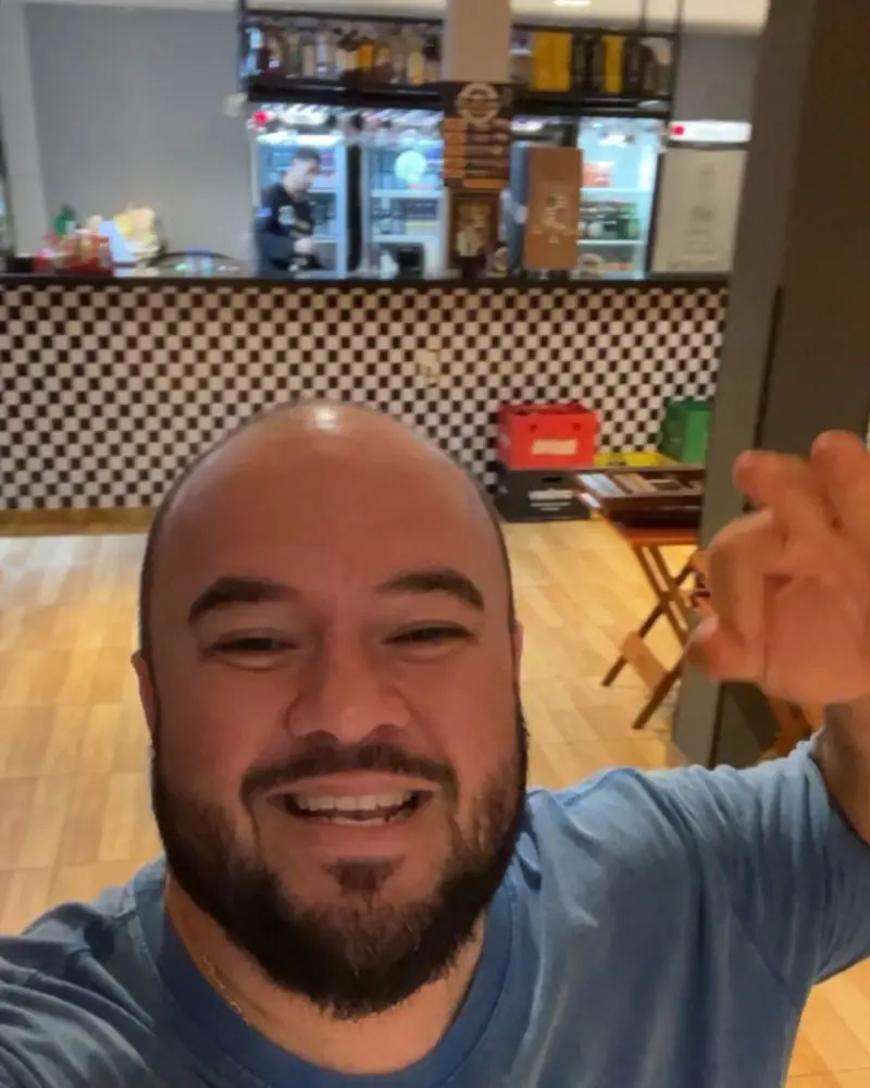 O dono do Boteco do Gude no salão, com o balcão xadrez e as geladeiras ao fundo