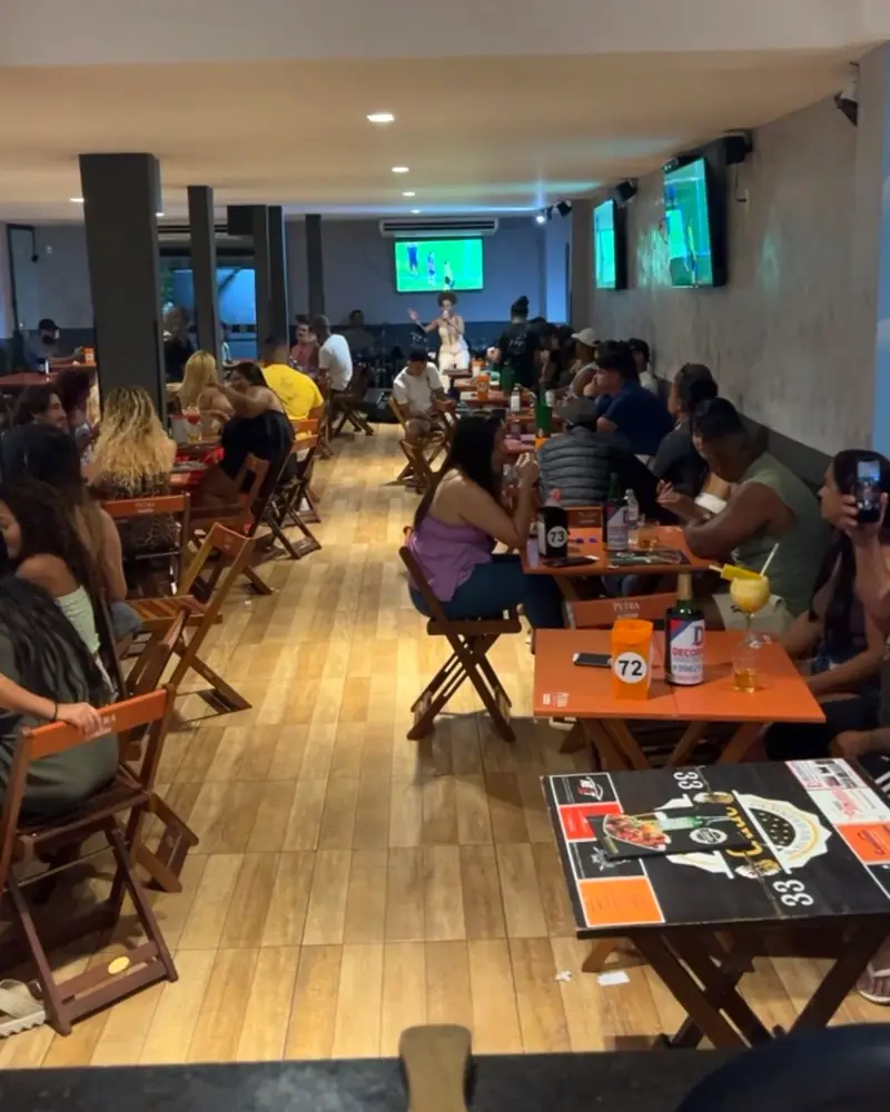 Salão do Boteco do Gude cheio numa noite de música ao vivo, com futebol nos telões